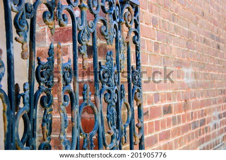Old forging gate with ornament (entry to abandoned manor) and red stone brick wall. Selective focus on the remote side of the fence.