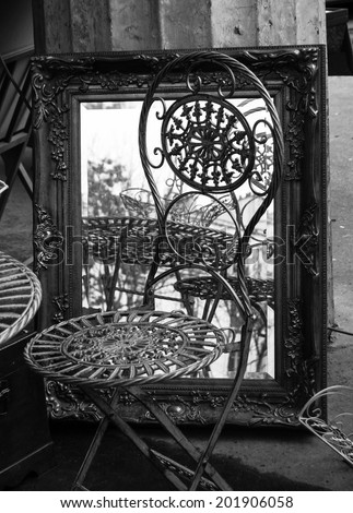 Chair and mirror in golden frame at flea market in Paris. Retro style postcard. Aged photo. Black and white.