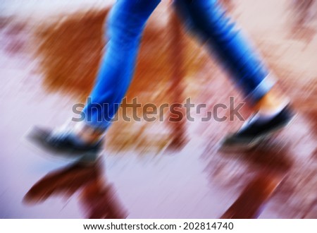 Blurred walking legs in motion on the wet brown with reflection in rainy day.