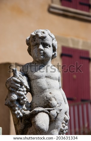Statue of Bacchus (Dionysus) with grapes in his hands. Garden sculpture and old stone house with maroon wooden shutters at backgrounds. (Chateauneuf du Pape, Provence, France)