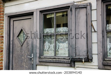 A front of the house. A door and a window with white lace curtain decorated with windmill and tree pattern and wooden hinged shutters . (Amiens, Picardy, France)  Rustic background.