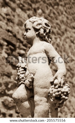 Statue of Bacchus (Dionysus) with grapes in his hands against rough stone wall. Garden sculpture. (Chateauneuf du Pape, Provence, France) Aged photo. Sepia.