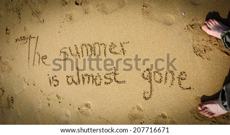 A sentence written on the sand of a beach: THE SUMMER IS ALMOST GONE, footprints and female foots . Vacation end / back from holiday / back to the work or school concept. Vignette effect.