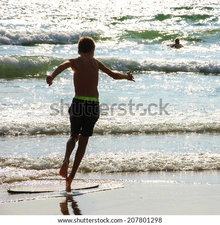 Boy moves on the surf board (alongside the sea shore) and a man swimming in the waves. Back view. (Brittany, France)
