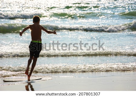 Boy moves on the surf board (alongside the sea shore) at sunset. Back view. (Brittany, France). Freedom concept.