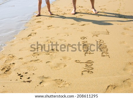 A sentence written on the sand of a beach: THE SUMMER IS ALMOST GONE, footprints and male and little boy foots . Vacation end / back from holiday / back to the work or school concept.
