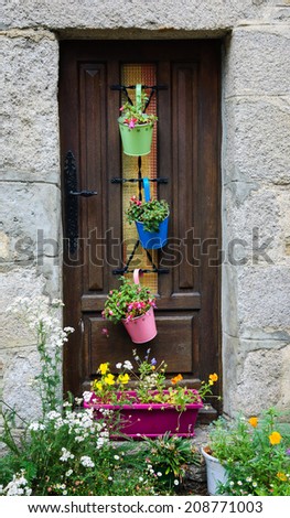 A wooden house door decorated with three colorful metal pots (with carved floral pattern)  with fuchsia flowers. Historic town Moncontour. Brittany, France