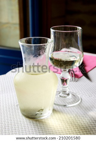 Misted pitcher with cold white wine and one glass on paper tablecloth in simple rustic restaurant.