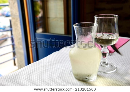 Misted pitcher with cold white wine and one glass on paper tablecloth in simple rustic restaurant. Opened door to the balcony.