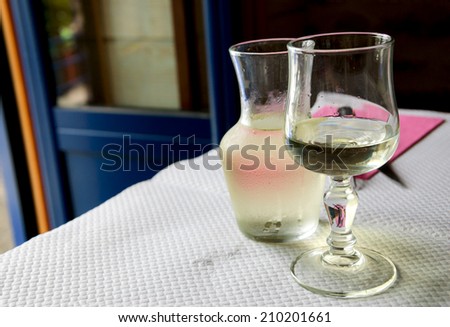 Misted pitcher with cold white wine and one glass on paper tablecloth in simple rustic restaurant. Selective focus on the wineglass.