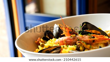 Seafood paella with chicken casserole and chorizo sausage in rustic restaurant. Opened blue door to the balcony.