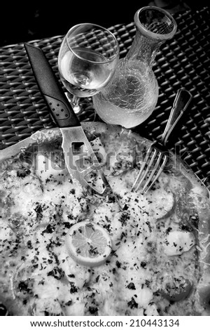 Delicious seafood pizza with scallops on wicker table in rustic pizzeria restaurant served with cold white wine in ornate pitcher. Retro aged photo. Black and white.