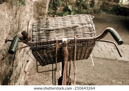 Rusty vintage bicycle with wicker basket leaning on a stone wall. Brittany, France. Closeup. Back view. Aged photo.