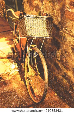 Rusty vintage bicycle with wicker basket leaning on a stone wall. Brittany, France.  A game of light and shadow. Aged photo.