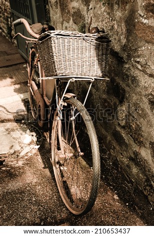 Rusty vintage bicycle with wicker basket leaning on a stone wall. Brittany, France. A game of light and shadow. Aged photo.