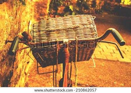 Rusty vintage bicycle with wicker basket leaning on a stone wall. Brittany, France. Closeup. Back view. Aged photo.