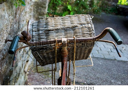 Rusty vintage bicycle with wicker basket leaning on a stone wall. Brittany, France. Closeup. Back view.