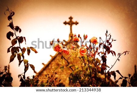 Cross and roses. A church in Dinan (Brittany, France). Selective focus on the flowers. Retro aged photo with scratches.