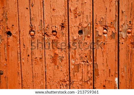 Texture of weathered wooden lining boards with peeling orange paint and rusty nail heads.
