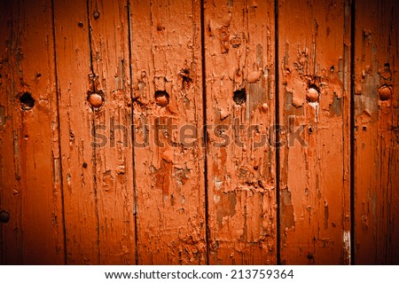 Texture of weathered wooden lining boards with peeling orange paint and rusty nail heads. Vignette.