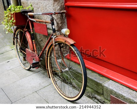 Rusty vintage red bicycle leaning with on red wooden board (useful for entering a text advertisement, menu etc) and carrying plants in wooden box as decoration.