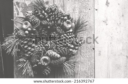 Vintage Christmas wreath with pine cones, sugared apples and red berries hanging on the grungy wooden door. Greeting card. Retro aged photo. Haze. Black and white.