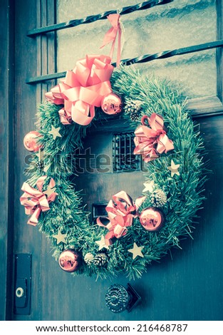 Christmas wreath with pine cones, pink bows, balls and golden stars hanging on the wooden door. Greeting card. Toned photo.