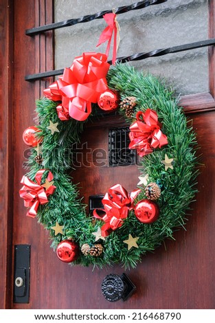 Christmas wreath with pine cones, red bows, balls and golden stars hanging on the wooden door. Greeting card.