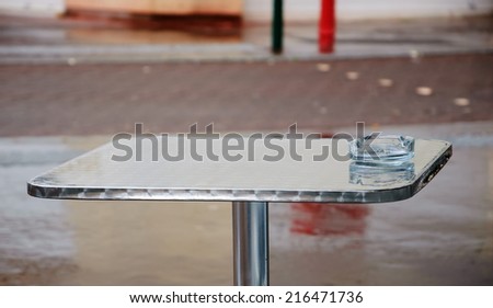 Terrace of a cafe after the rain. Empty glass ashtray on the table. Paris, France.