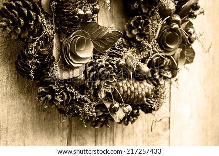 Vintage Christmas wreath with pine cones, flowers and red berries hanging on the grungy wooden door.  Greeting card. Aged photo. Sepia.