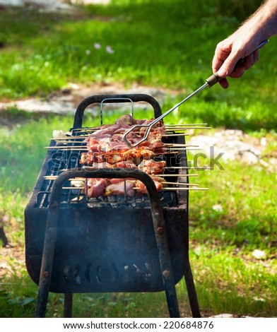 Man cooking marinated turkey shashlik on wooden skewer on the grill. Backyard party background.