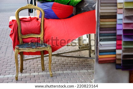 Colorful upholstery samples and wooden frame of  antique armchair near the entry to the workshop. Beersheba, Israel. Selective focus on the chair.