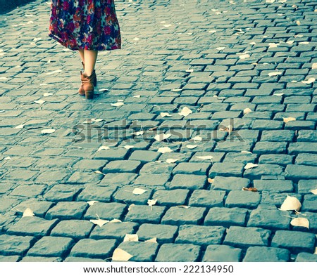Closeup of young woman legs on Parisian cobblestone street covered with yellow autumn leaves. Retro aged photo.