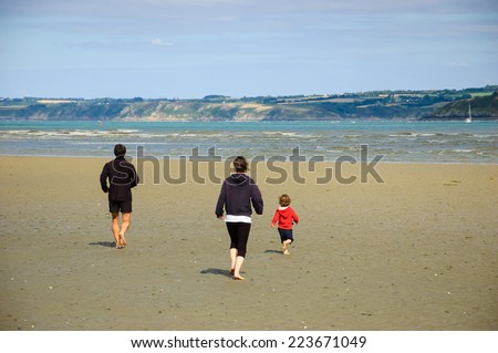 Young family (mother, father and little child) running towards the sea. Back view. Brittany, France.