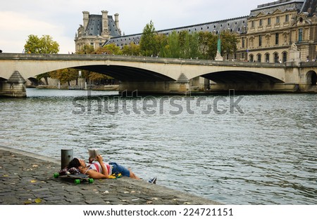 PARIS, FRANCE - OCTOBER 4, 2014: Unidentified young man laying on his skateboard and reading on Seine bank near Louvre museum. Seine embankment is very popular promenade at weekends.