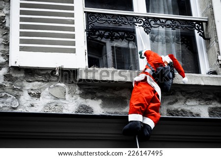 Santa Claus climbing up a wall into a window. Traditional Christmas decoration. Aged photo.