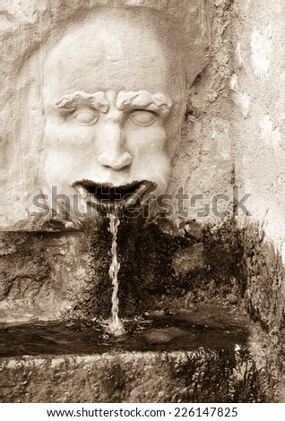 Fountain in medieval village Colmars (Alpes-de-Haute-Provence, France). Man with water coming out of  his mouth. Aged photo. Sepia.