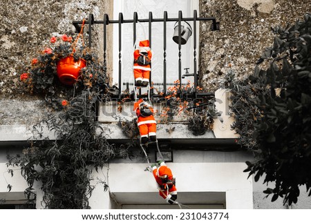 Three Santa Claus figures climbing up a wall into a window. Traditional Christmas decoration. Aged photo.