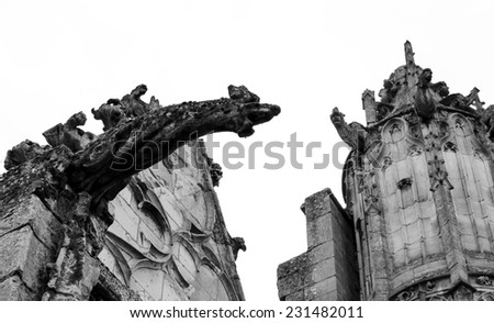 Terrible stone gargoyle on the facade of Senlis cathedral. France. Aged photo. Black and white.
