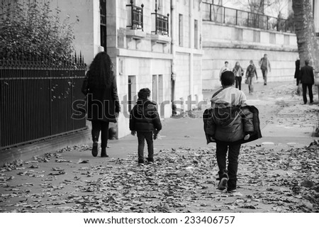 Autumn in Paris. Woman and two kids (mother and sons) walking over the faded plane-tree leaves covered pavement on typical Parisian street. Aged photo. Black and white.