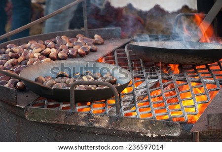 Chestnuts roasted in old iron pans over the fire at traditional Christmas medieval fair in Provins (France). Selected focus on the grill and on the burned chestnuts in the pan.