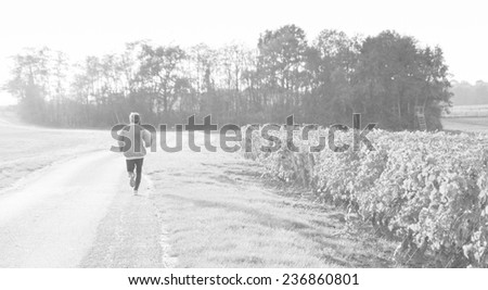 A mid aged man running at sunset near the vineyard. Autumn in Loire Valley (Val de Loire, France) Retro aged photo. Black and white.