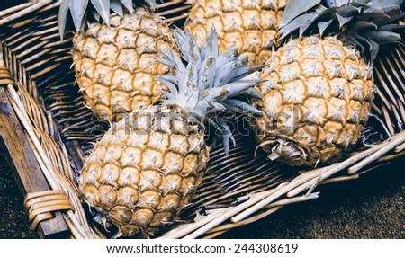 Pineapples in wicker basket at organic farmers market in Paris (France). Aged photo.