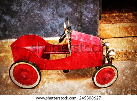 Red vintage toy car near entrance to the house. Side view. Retro aged photo with scratches.