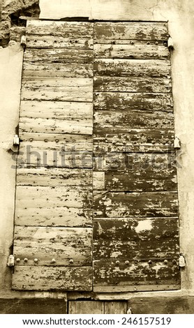 Closed wooden shutters with peeling paint and nail heads. Stucco wall house. Aged photo. Sepia.
