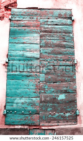Closed wooden shutters with peeling paint and nail heads. Stucco wall house.