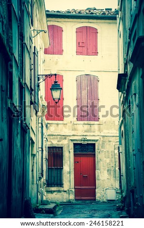 Narrow the street in Arles (Provence, France). Weathered stucco walls, red wooden shutters and forging lanterns. Aged photo.