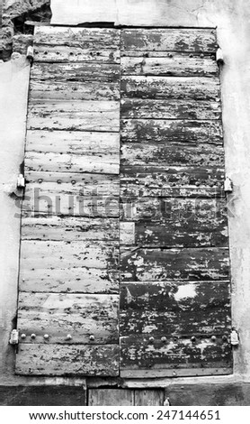 Closed wooden shutters with peeling paint and nail heads. Stucco wall house. Aged photo. Black and white.