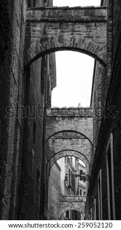 Arches over the narrow street in Venice.  A game of light and shadow. Aged photo. Black and white.