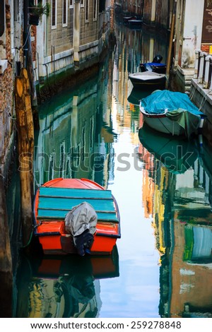 Narrow canal in Venice. Boats and reflection of colorful houses in the water. Selective focus on the  reflection.